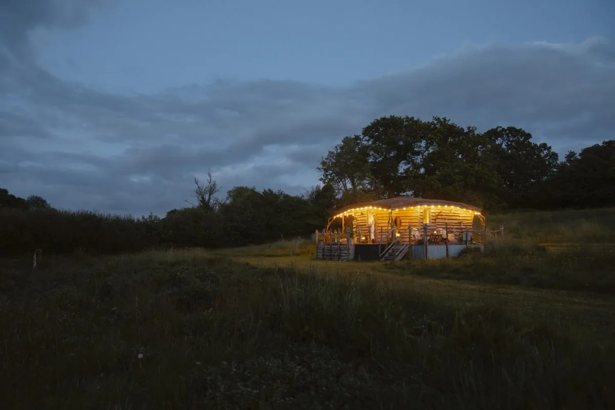 Nighttime view of a meadow with the cabin illuminated with festoon lights - Luxury Glamping Cabin Carmarthenshire, West Wales
